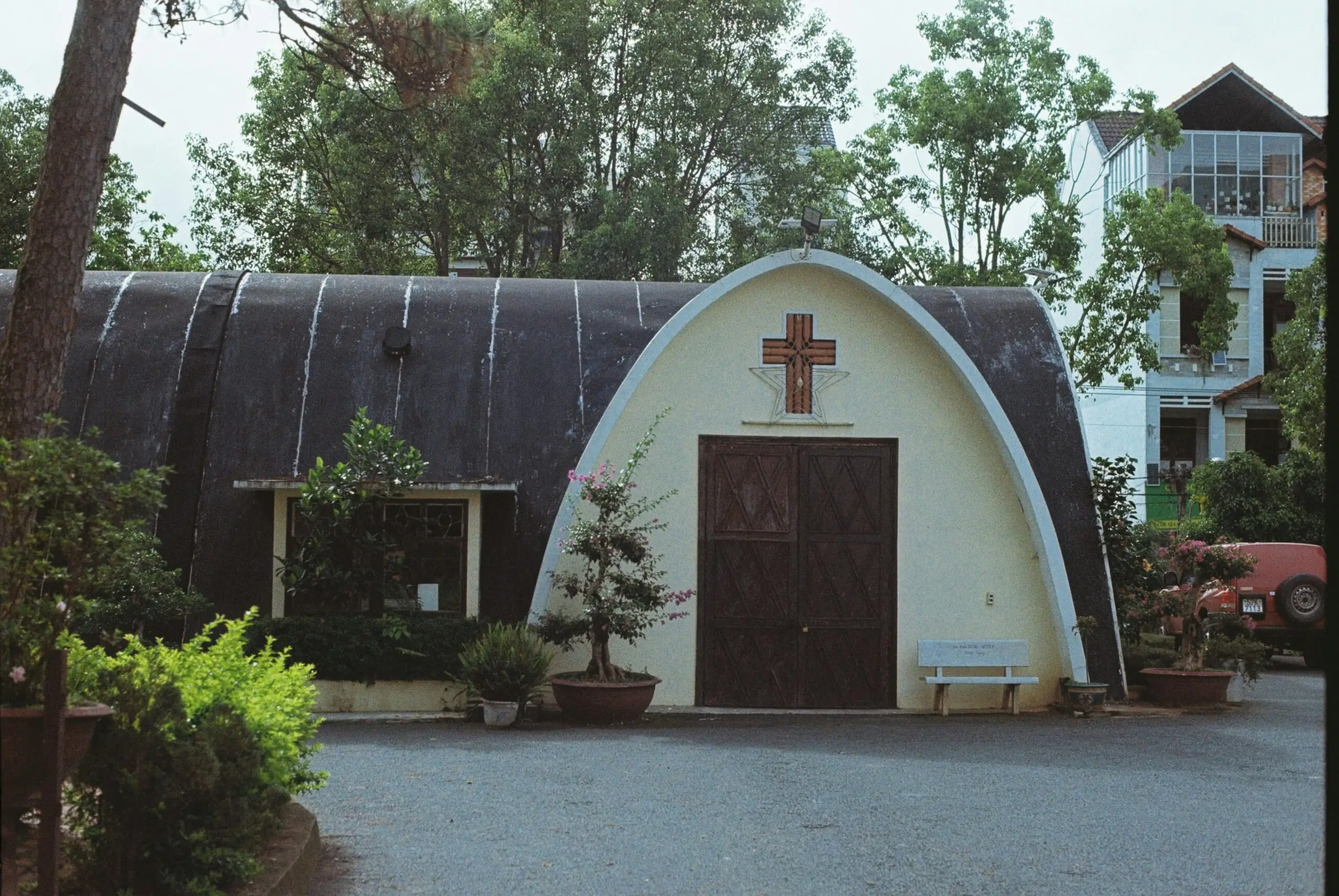 A small chapel with an arched roof and prominent cross, surrounded by greenery.
